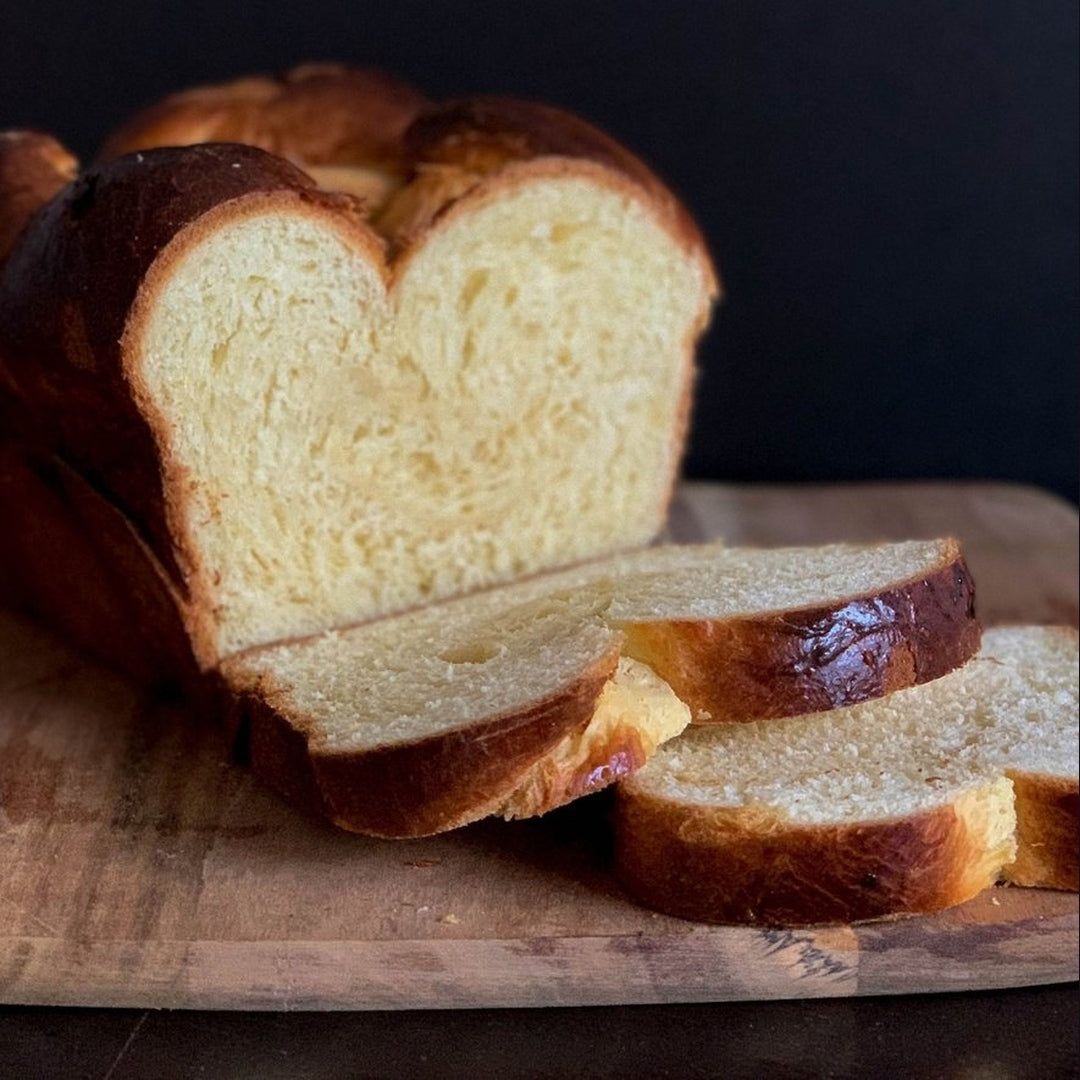 Sweet brioche loaf on a wooden board with several slices fanned out.
