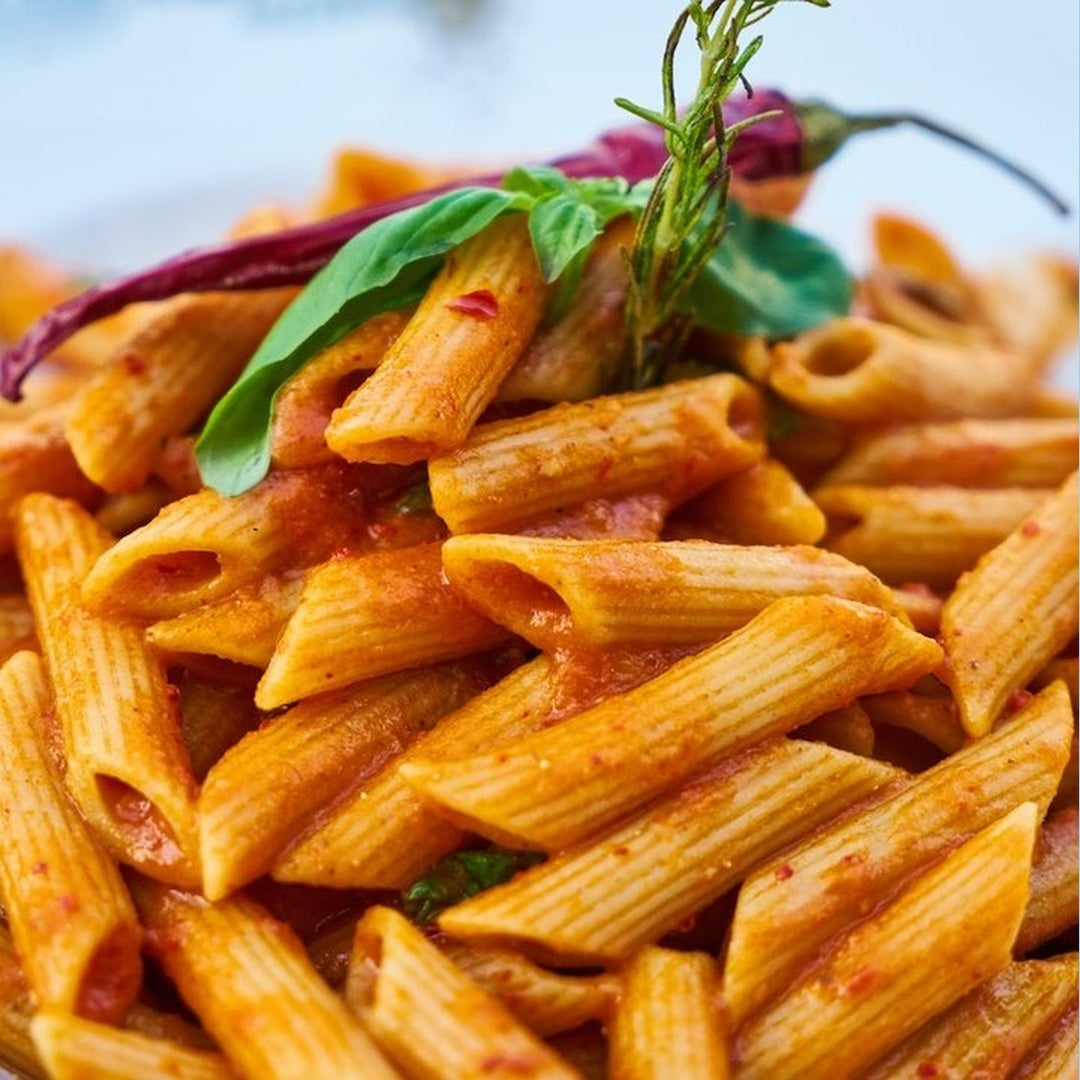 Penne pasta in roasted pepper tomato sauce with a rosemary garnish.