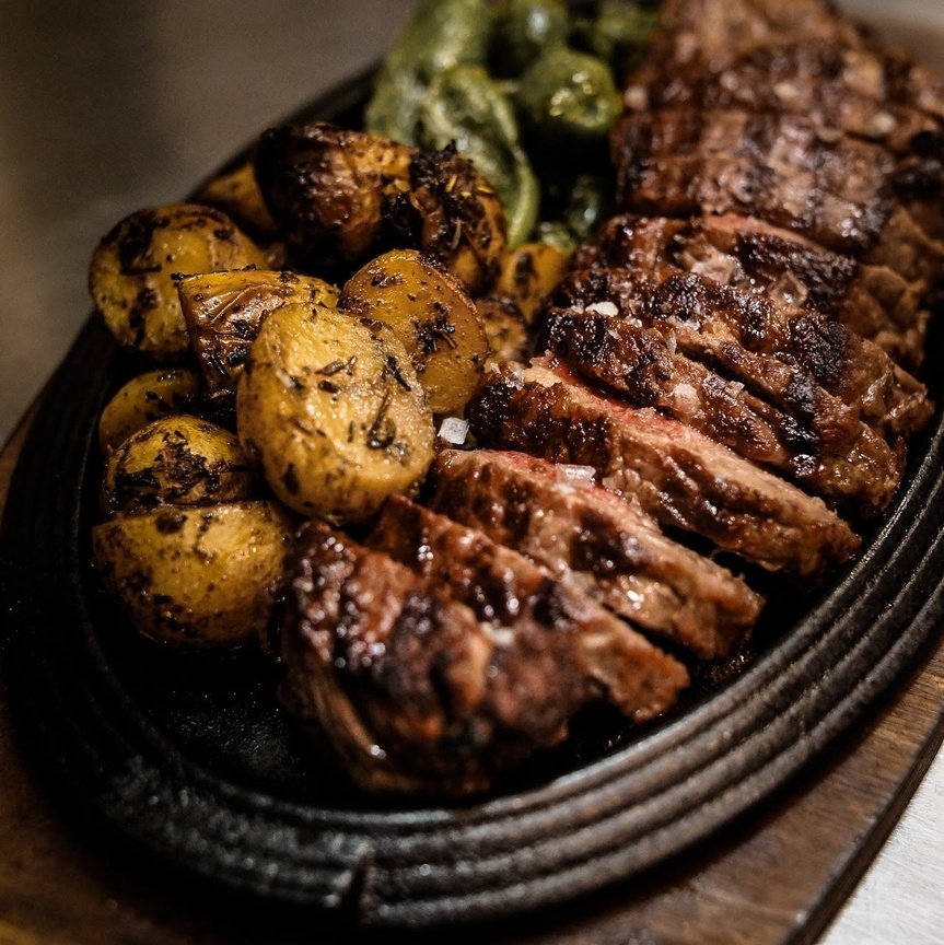 Grilled ribeye steak slices with crispy roasted potatoes on a sizzling platter
