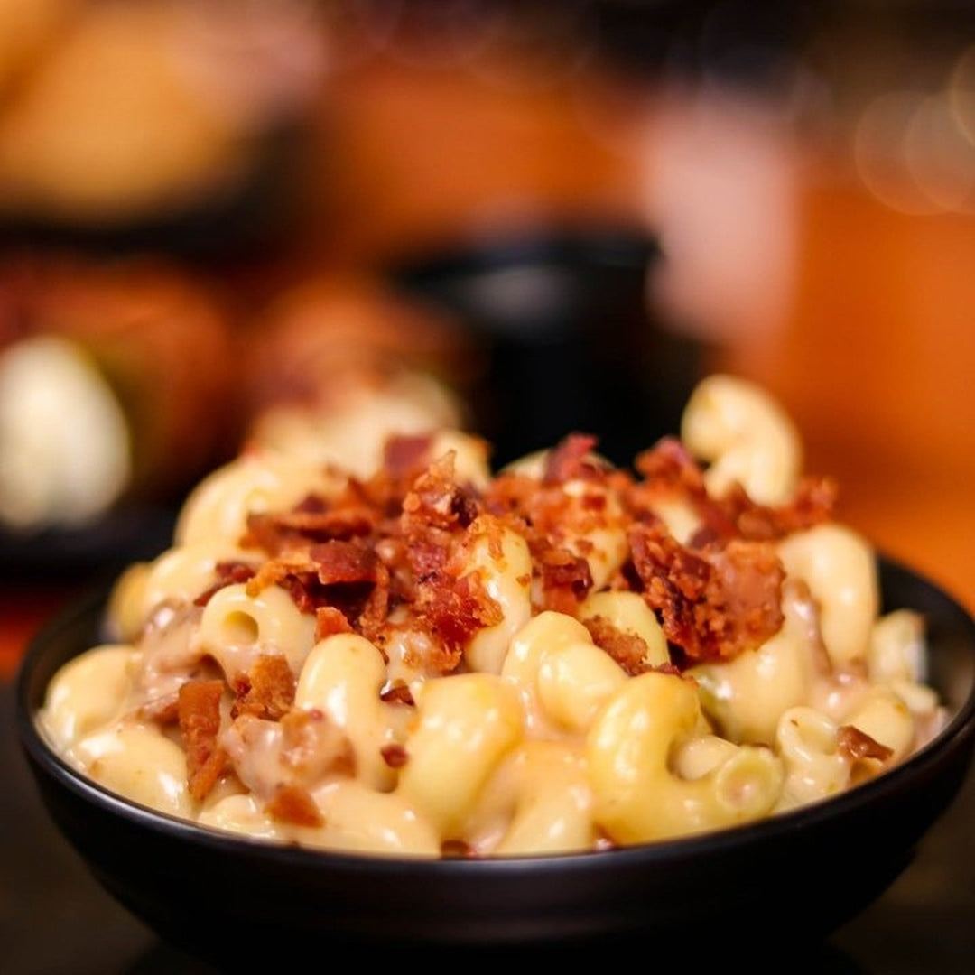 Creamy macaroni and cheese topped with crispy bacon bits in a black bowl