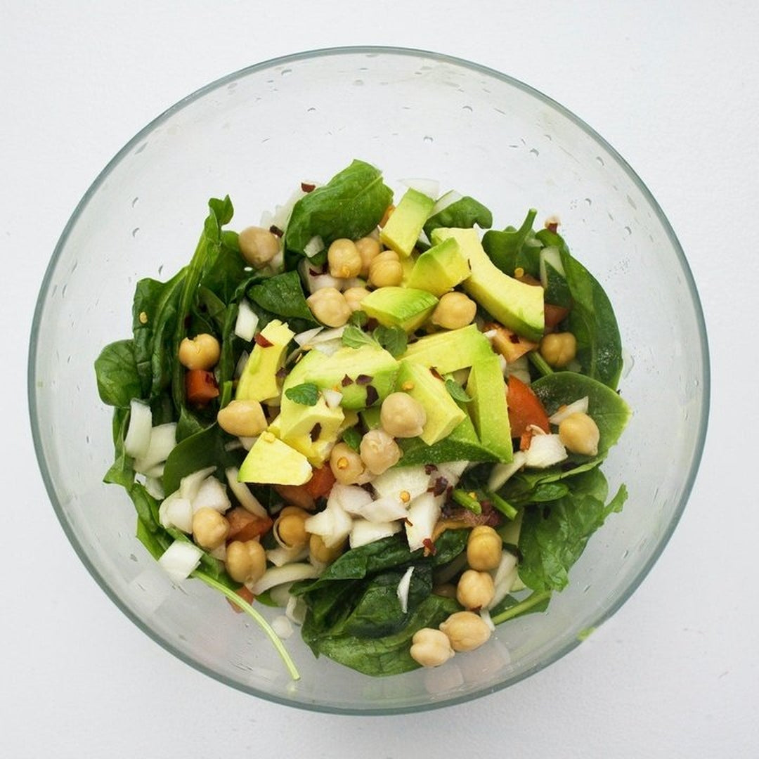 Chickpea salad with avocado and greens in a clear glass bowl