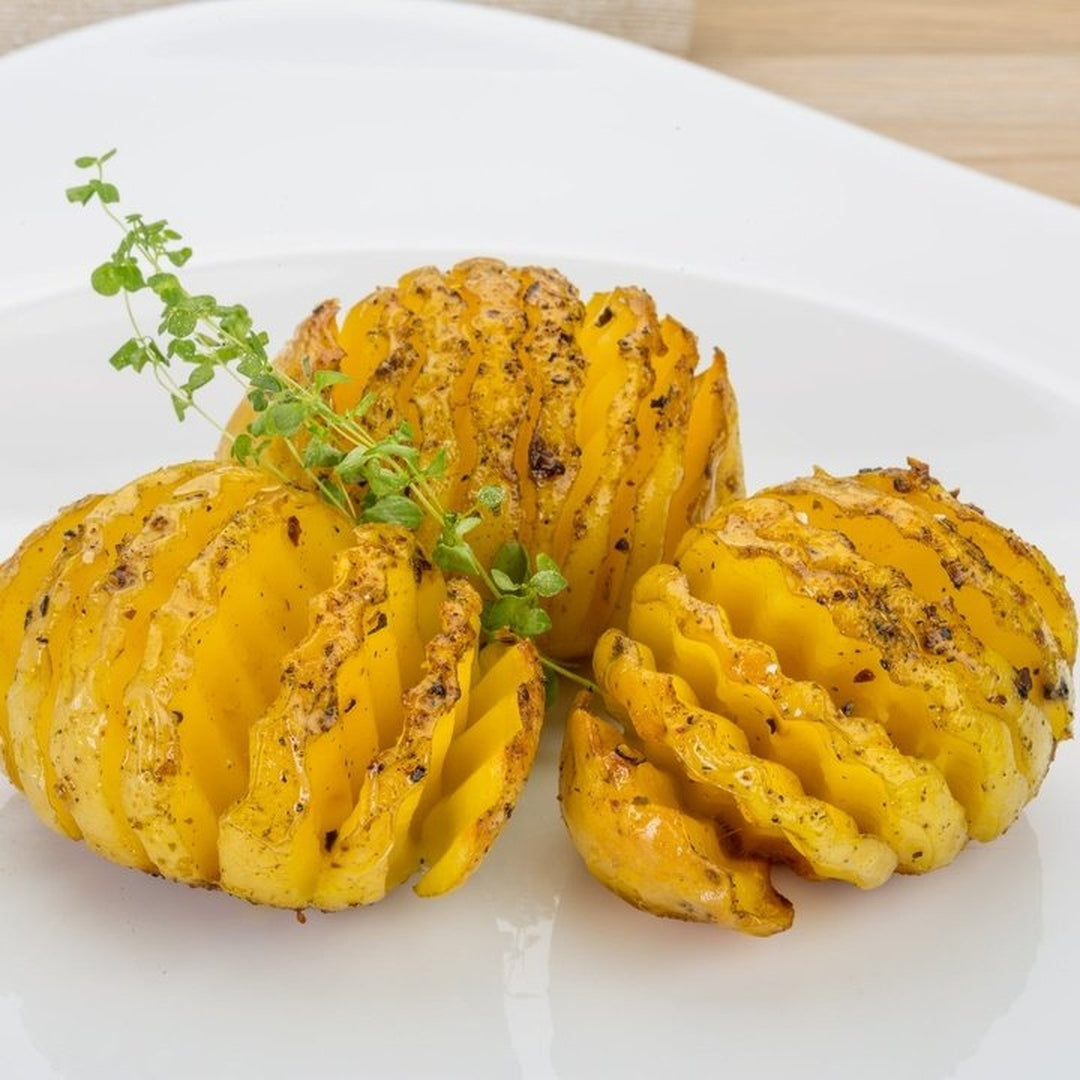 Cheesy Hasselback potatoes arranged on a white plate with a sprig of fresh herbs.