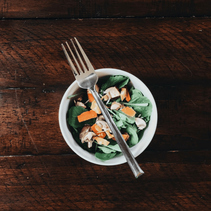 Top view of Irish flag salad showcasing spinach, pears, oranges, feta, and pistachios with a fork on a dark wooden table.
