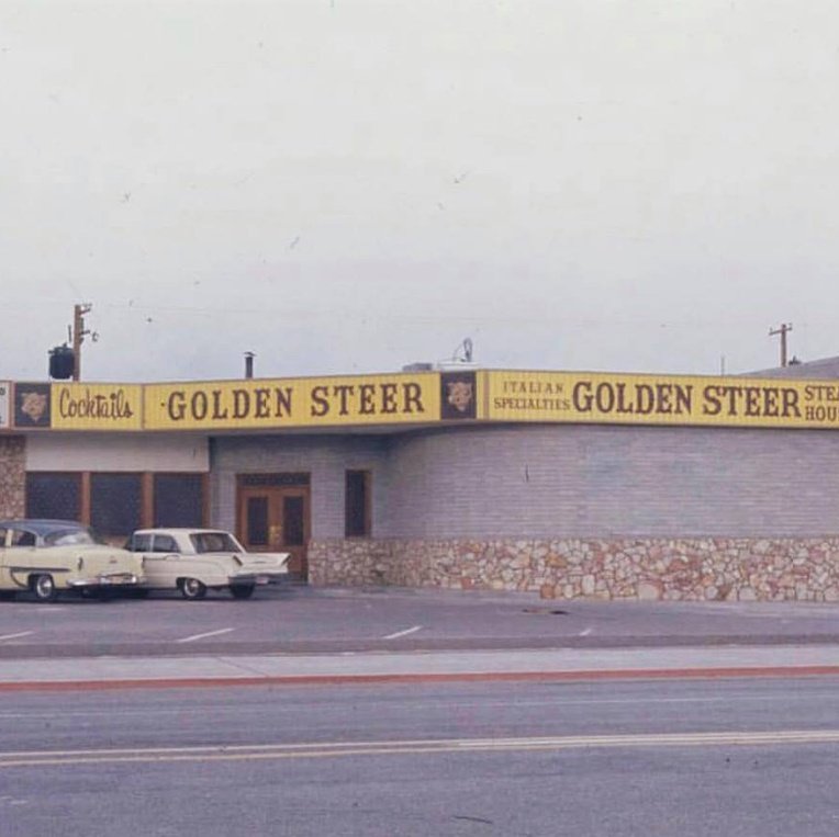 Vintage Golden Steer exterior with signage: Cocktails, GOLDEN STEER, ITALIAN SPECIALTIES, STEAK HOUSE — two classic cars.