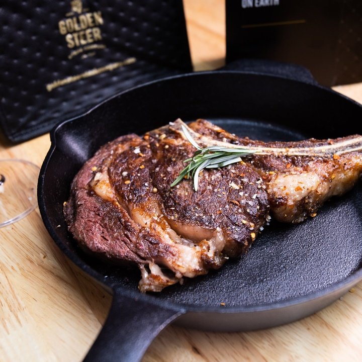 Bone-in ribeye in a cast-iron skillet, garnished with rosemary; background text reads GOLDEN STEER and ON EARTH.