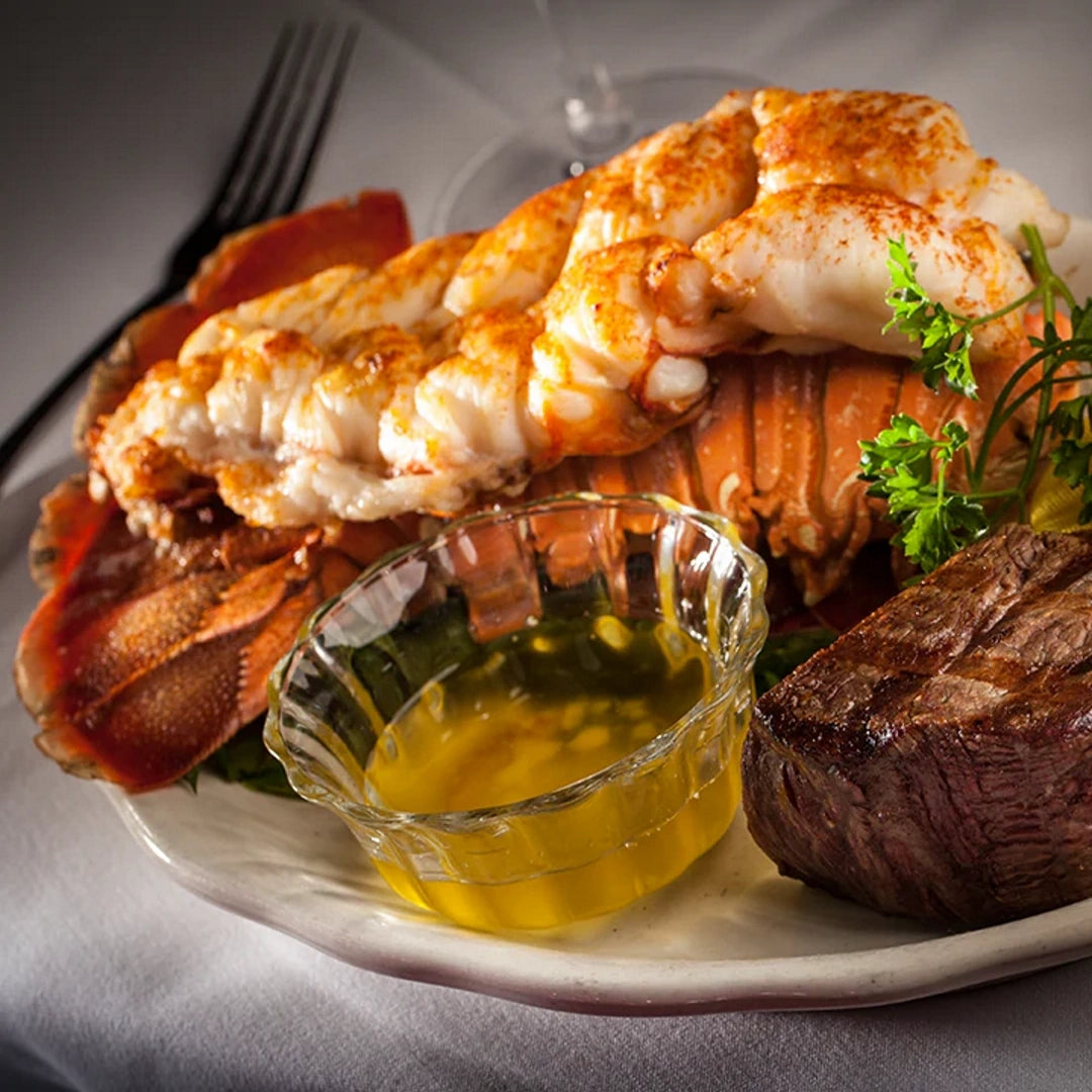 Grilled lobster tail with steak and a glass dish of melted butter on a white plate.