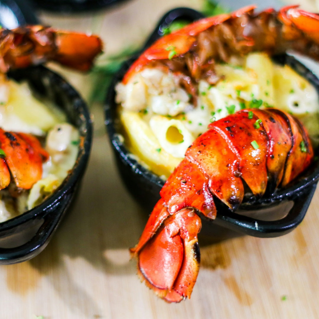 Grilled lobster tail served atop creamy macaroni in a small cast-iron dish.