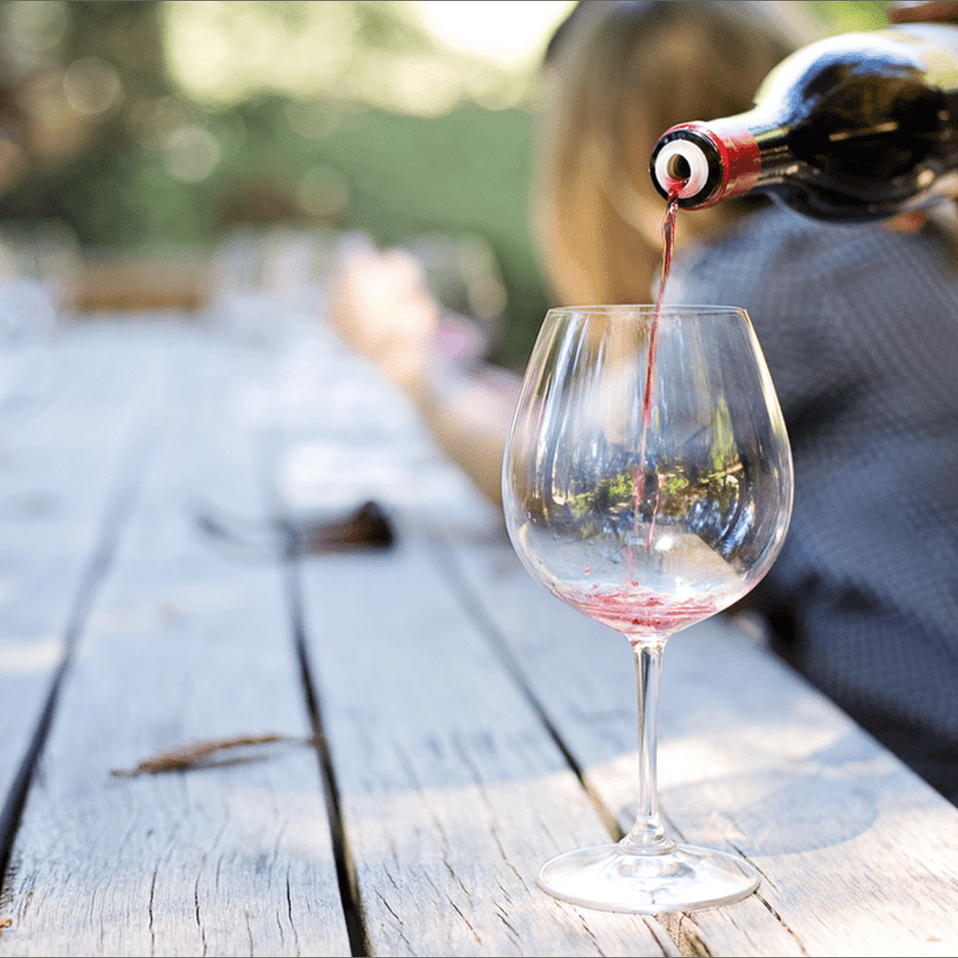 Red wine being poured into a glass on a weathered outdoor picnic table