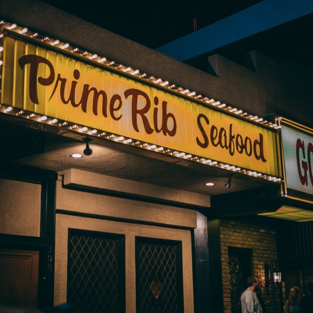 Yellow marquee reading ‘Prime Rib Seafood’ glowing over the Golden Steer entrance at night with people by the doorway