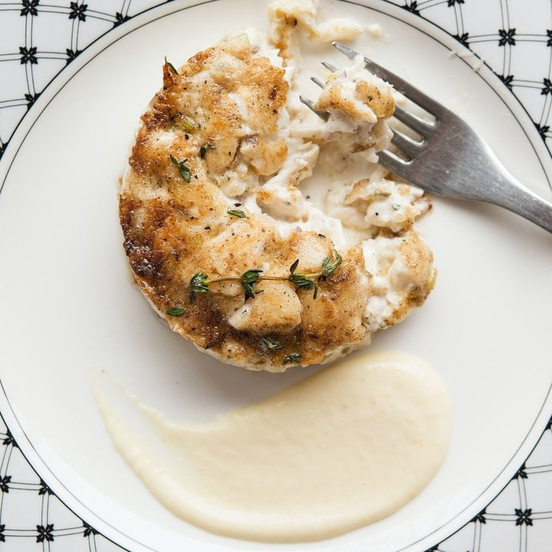 Crispy crab cake with herbs on a white plate with a creamy sauce.