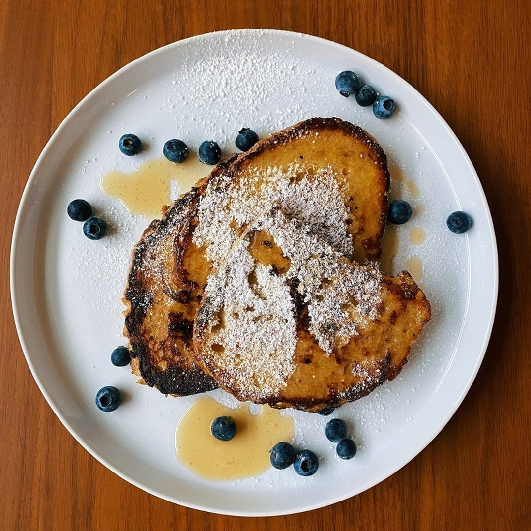 Challah French toast on a white plate with blueberries and maple syrup drizzle