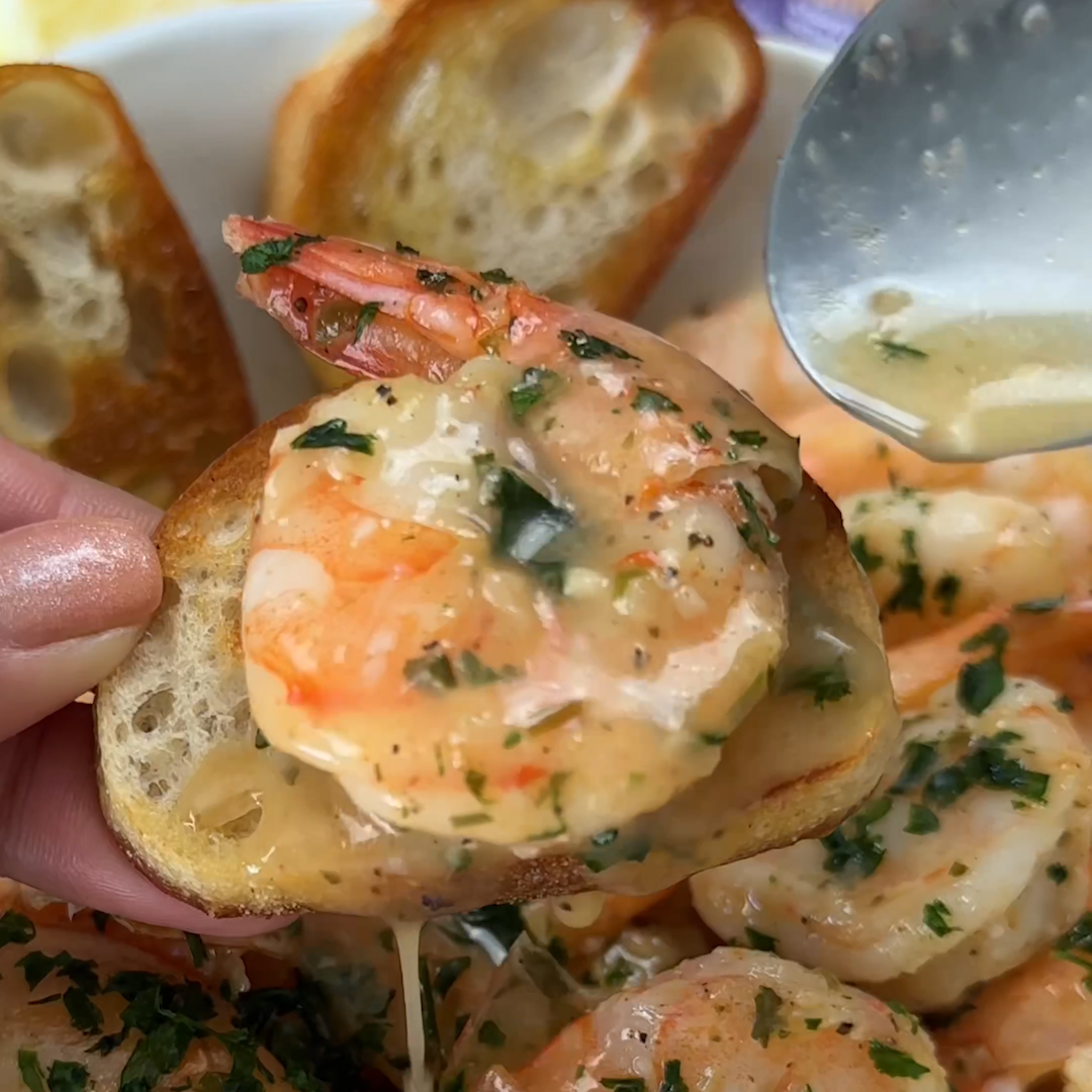 Close-up of garlic shrimp being spooned with De Jonghe butter sauce onto toasted bread crostini, garnished with parsley