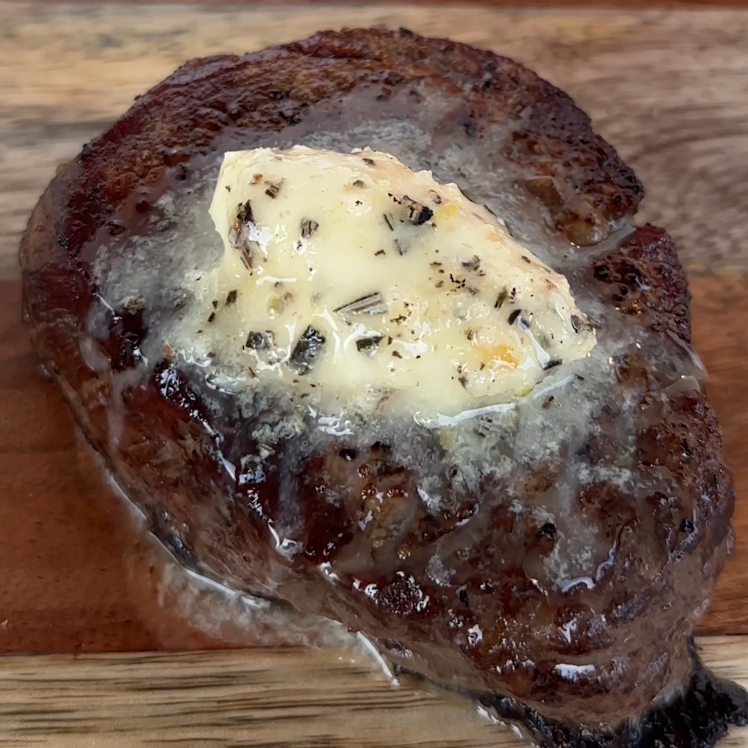 Seared filet mignon topped with melting herbed compound butter on a wooden board