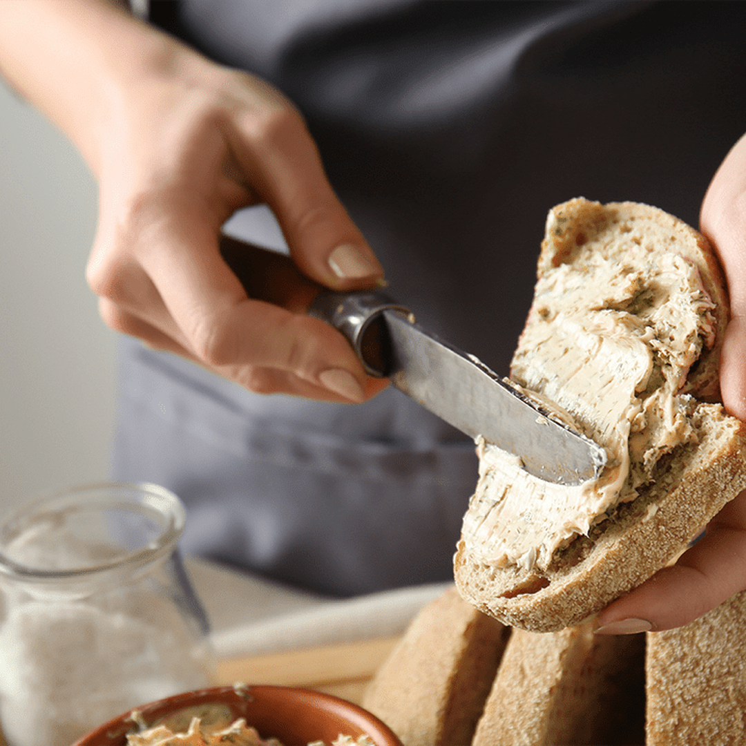 Hand spreading herbed butter on a slice of multigrain bread with a butter knife