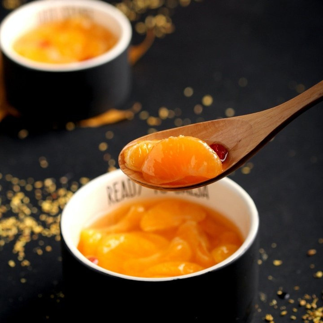 Glossy peach segments on a wooden spoon above a cup of peach compote with gold sprinkles; cup rim reads 'READY'
