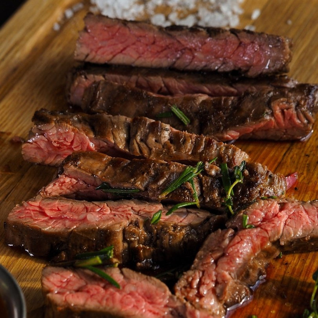 Sliced medium-rare grilled steak with rosemary on a wooden cutting board