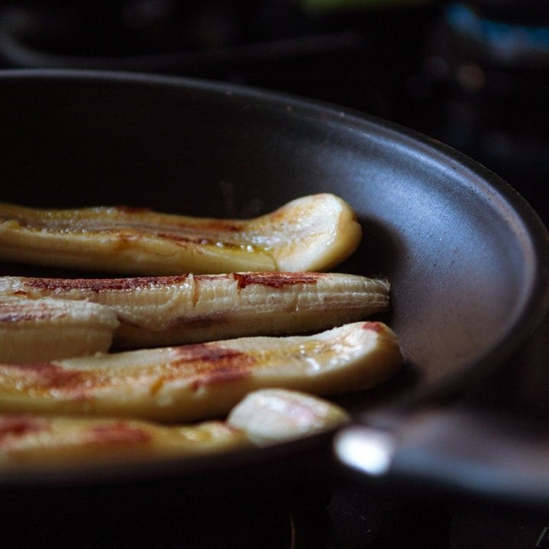 Halved bananas searing in a dark skillet, showing browned, caramelized edges
