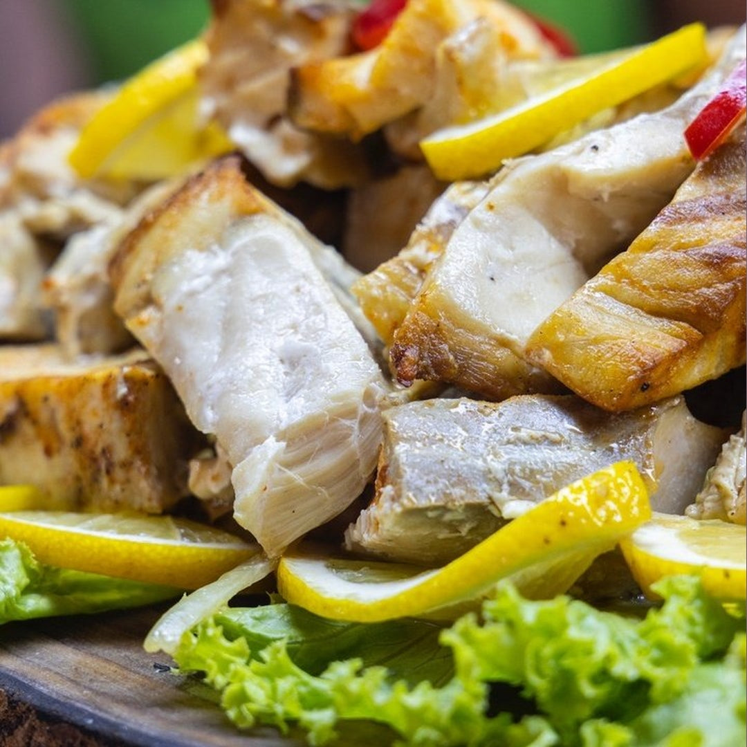 Sliced lemon-pepper mahi mahi fillets with lemon wedges on lettuce, lightly seared.