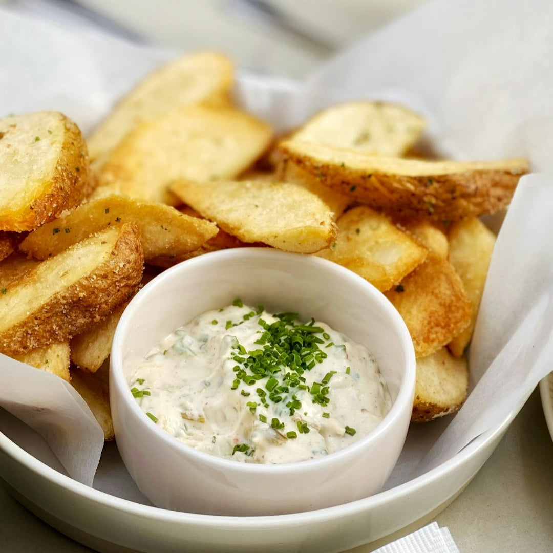 Caramelized onion dip topped with chopped chives in a small bowl, served with seasoned potato wedges