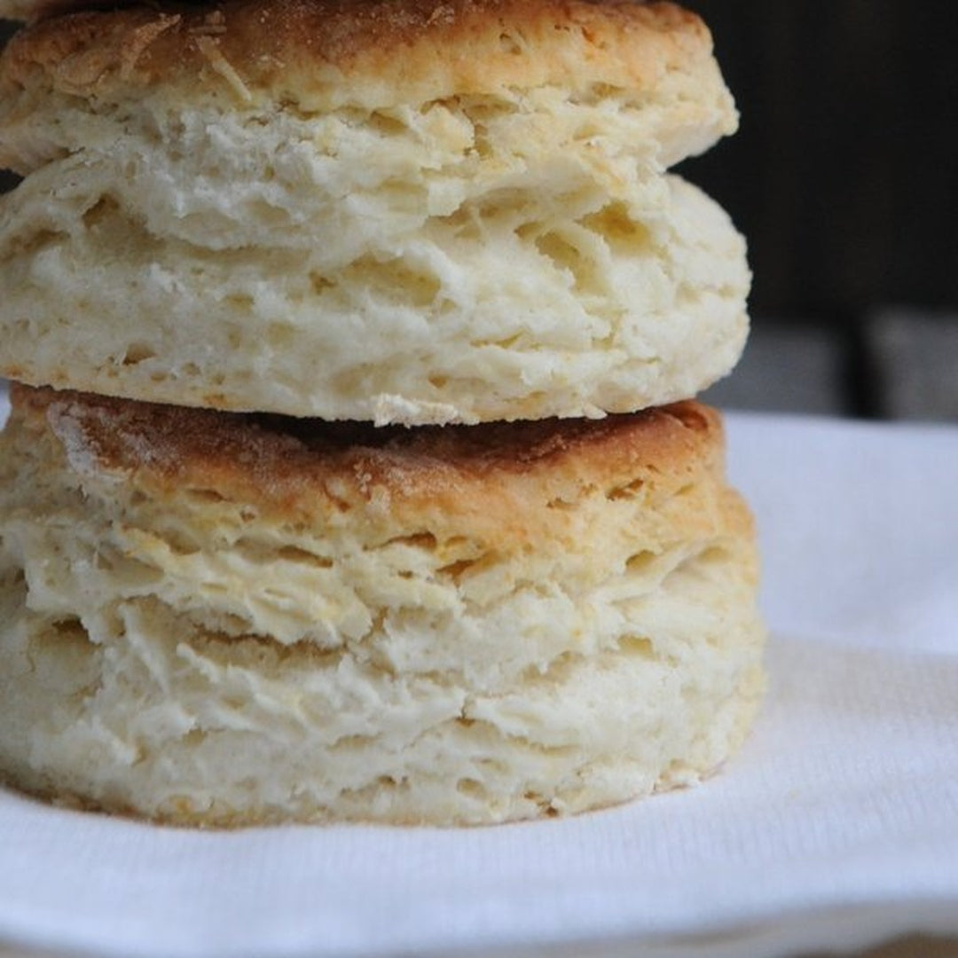 Two thick, flaky buttermilk biscuits stacked on a white napkin, golden-browned edges and layered interior.