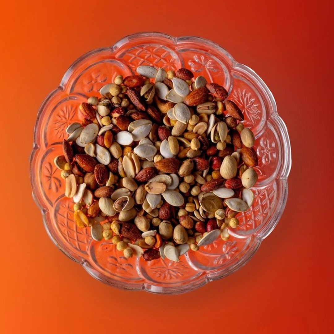 Top view of mixed roasted nut medley seasoned with Outlaw Rub in a cut-glass bowl on an orange background