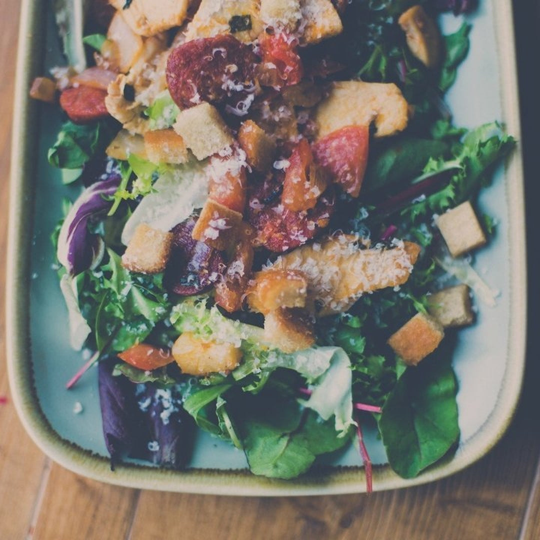 Mixed green salad with toasted croutons, grated cheese and tomato on a rectangular pale plate