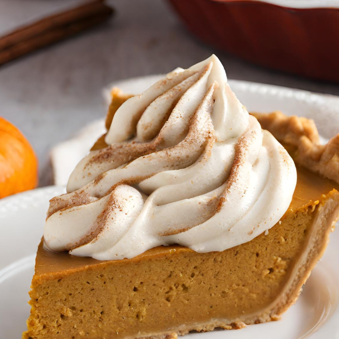 Slice of pumpkin pie topped with piped whipped cream dusted with cinnamon, on a white plate.