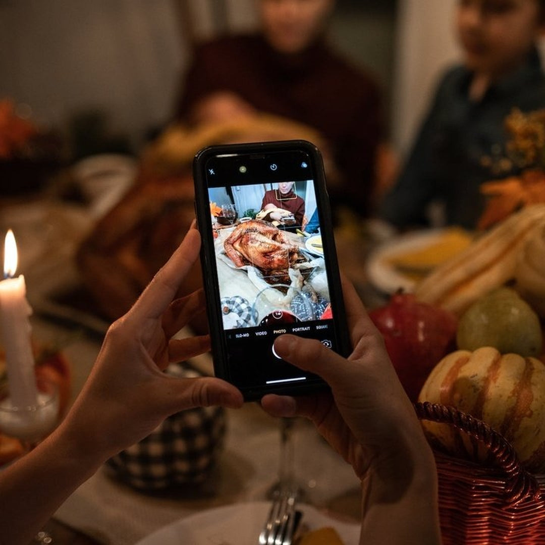 Hands hold a phone photographing a roasted turkey.