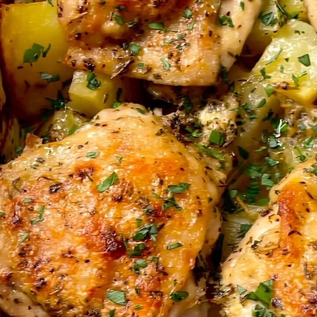 Close-up of golden roasted chicken thighs and cubed potatoes sprinkled with chopped parsley and seasoning.