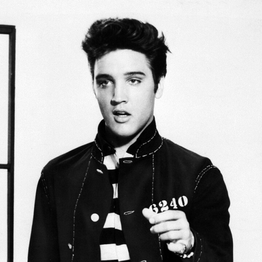 Elvis Presley wearing a dark jacket with the number 6240 over a striped shirt against a plain white background
