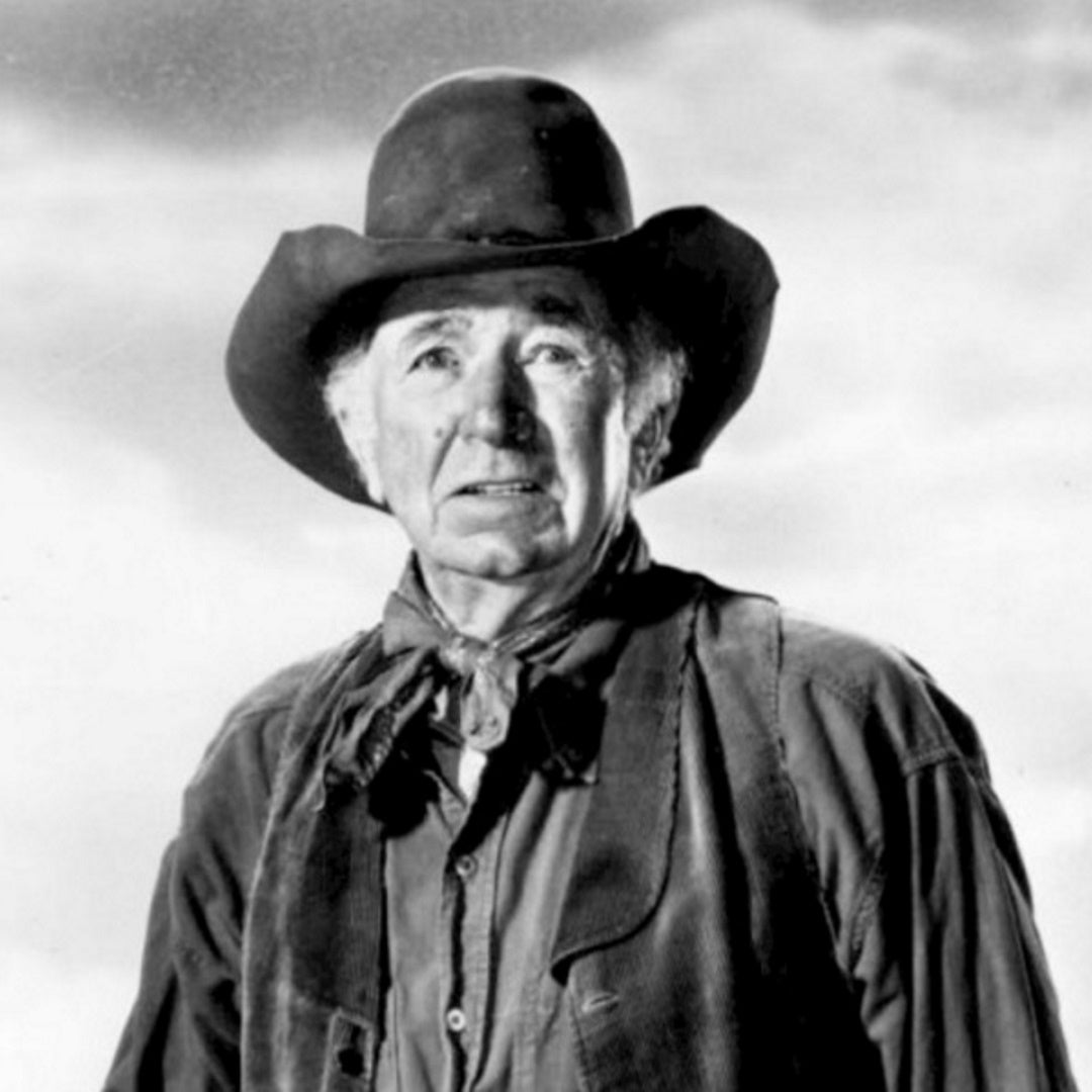 Walter Brennan in cowboy hat and neckerchief wearing a western jacket, three-quarter portrait against a cloudy sky.