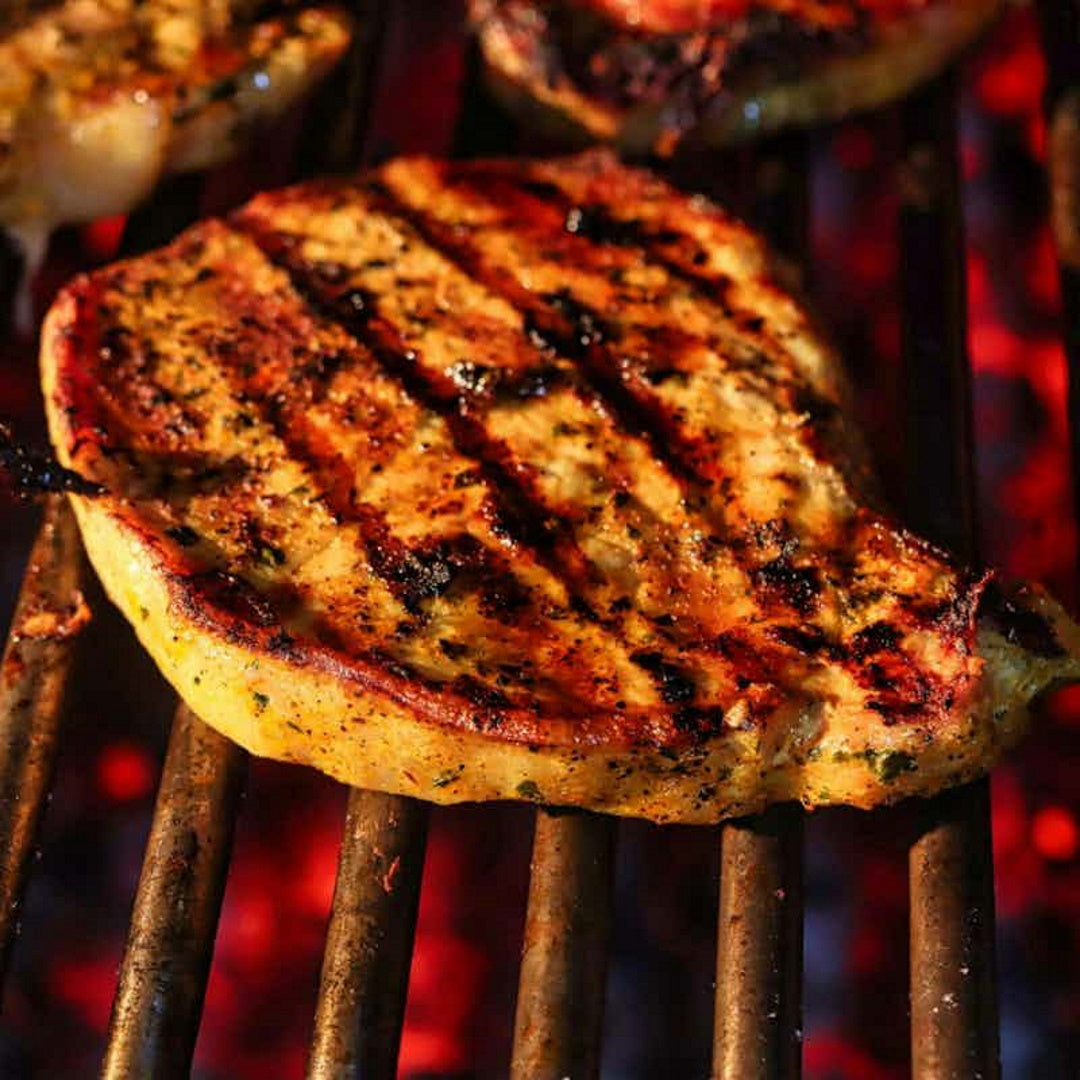 Close-up of a grilled steak showing charred sear marks, seasoning and a golden crust over a glowing charcoal grill
