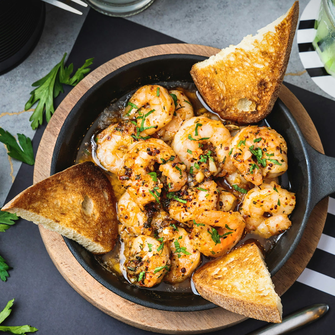Sautéed garlic shrimp in a hot skillet, butter sauce with parsley, served with toasted bread wedges.