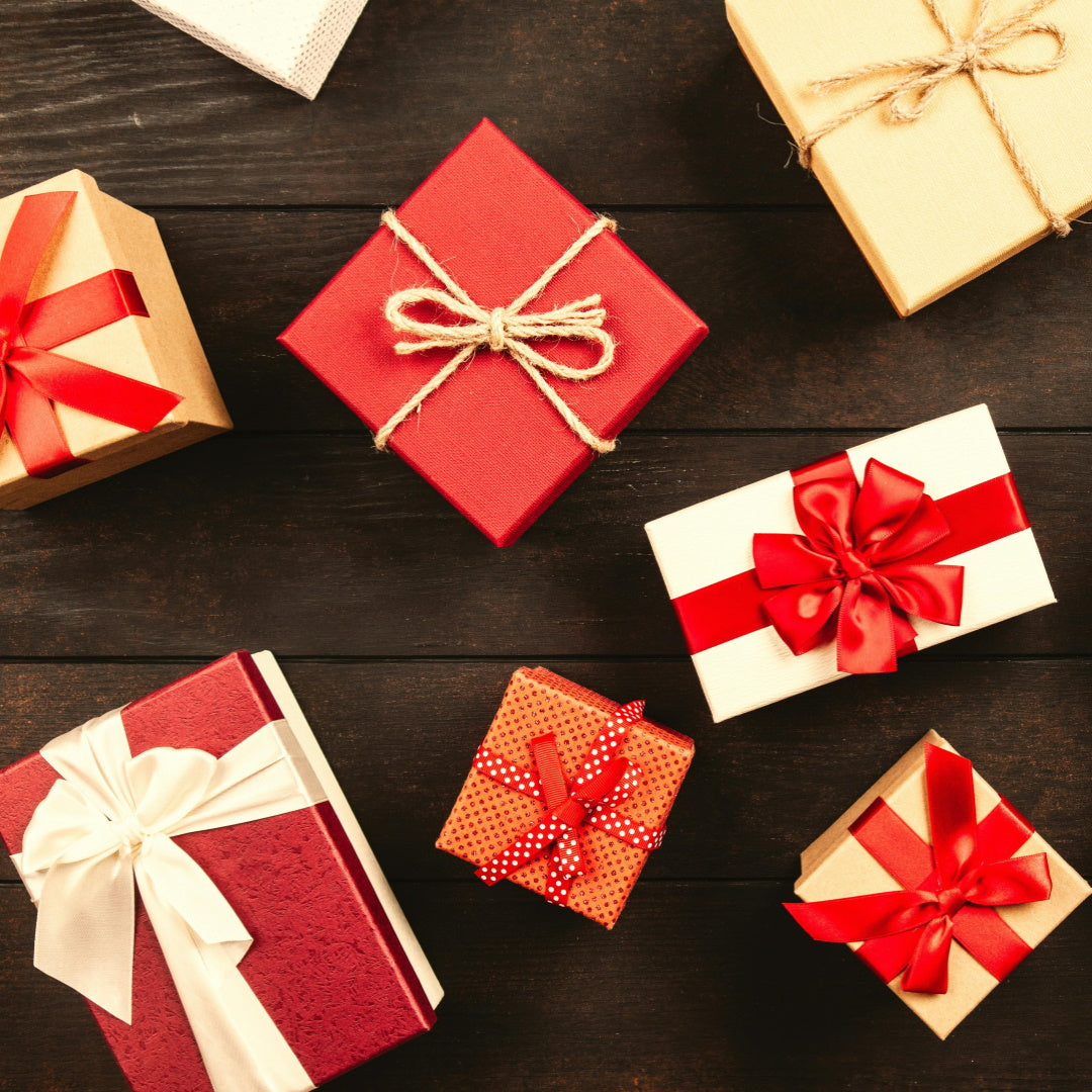 Assorted wrapped holiday gift boxes with red, cream, and kraft paper and ribbon bows on a dark wood background.