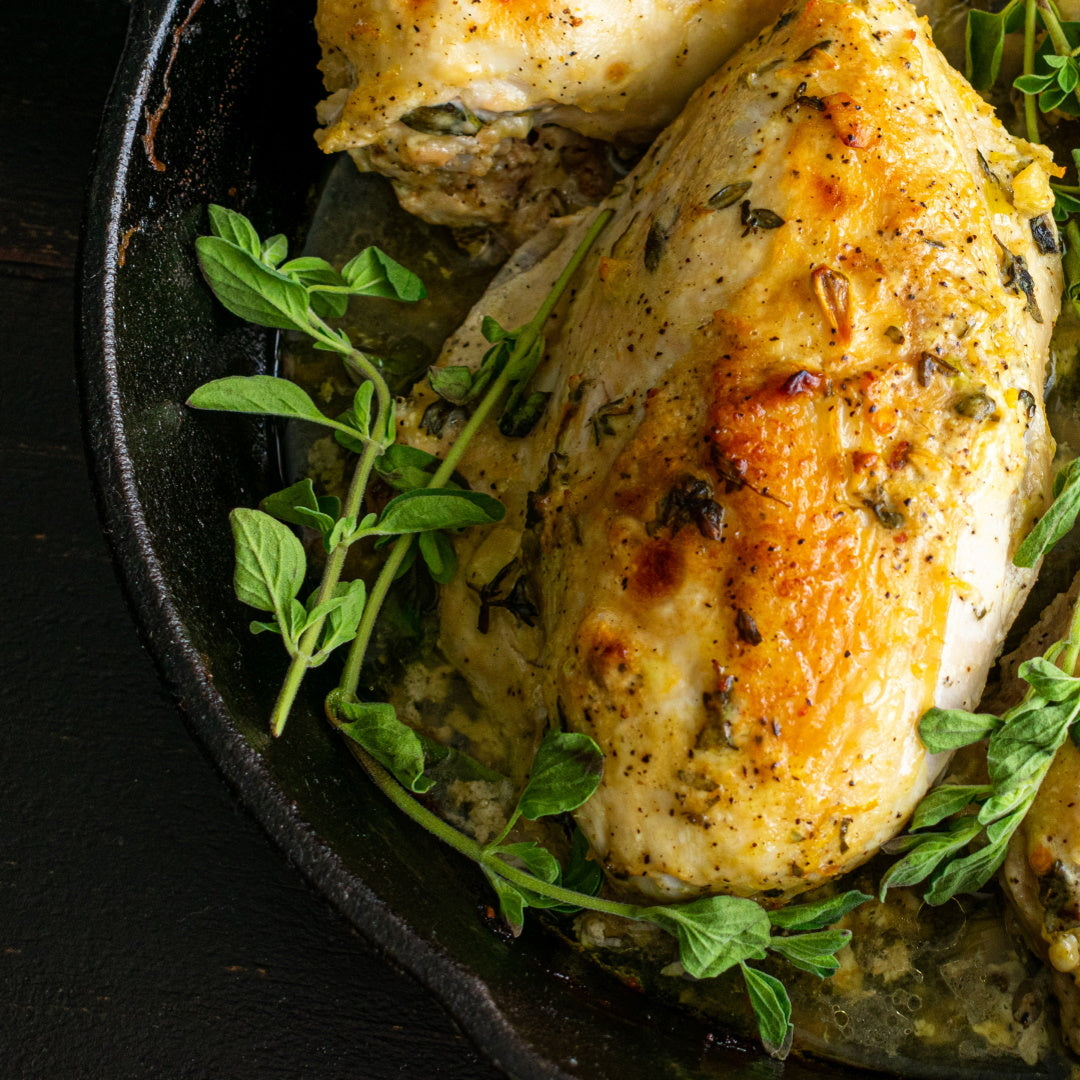 Roasted chicken breasts in a cast-iron skillet with fresh oregano sprigs