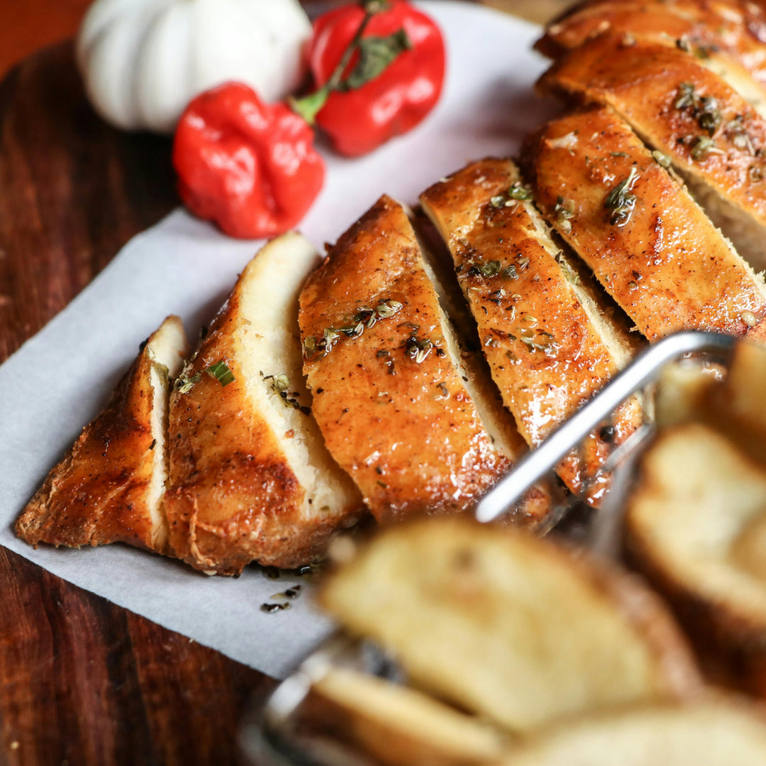 Sliced roasted garlic-herb chicken breast, glazed and sprinkled with herbs, on parchment with red peppers in the background.