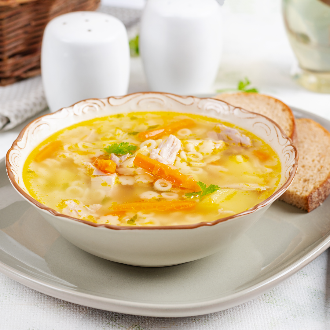 Bowl of pastina soup with tiny ring pasta, carrot strips and parsley, served with two slices of bread on a plate