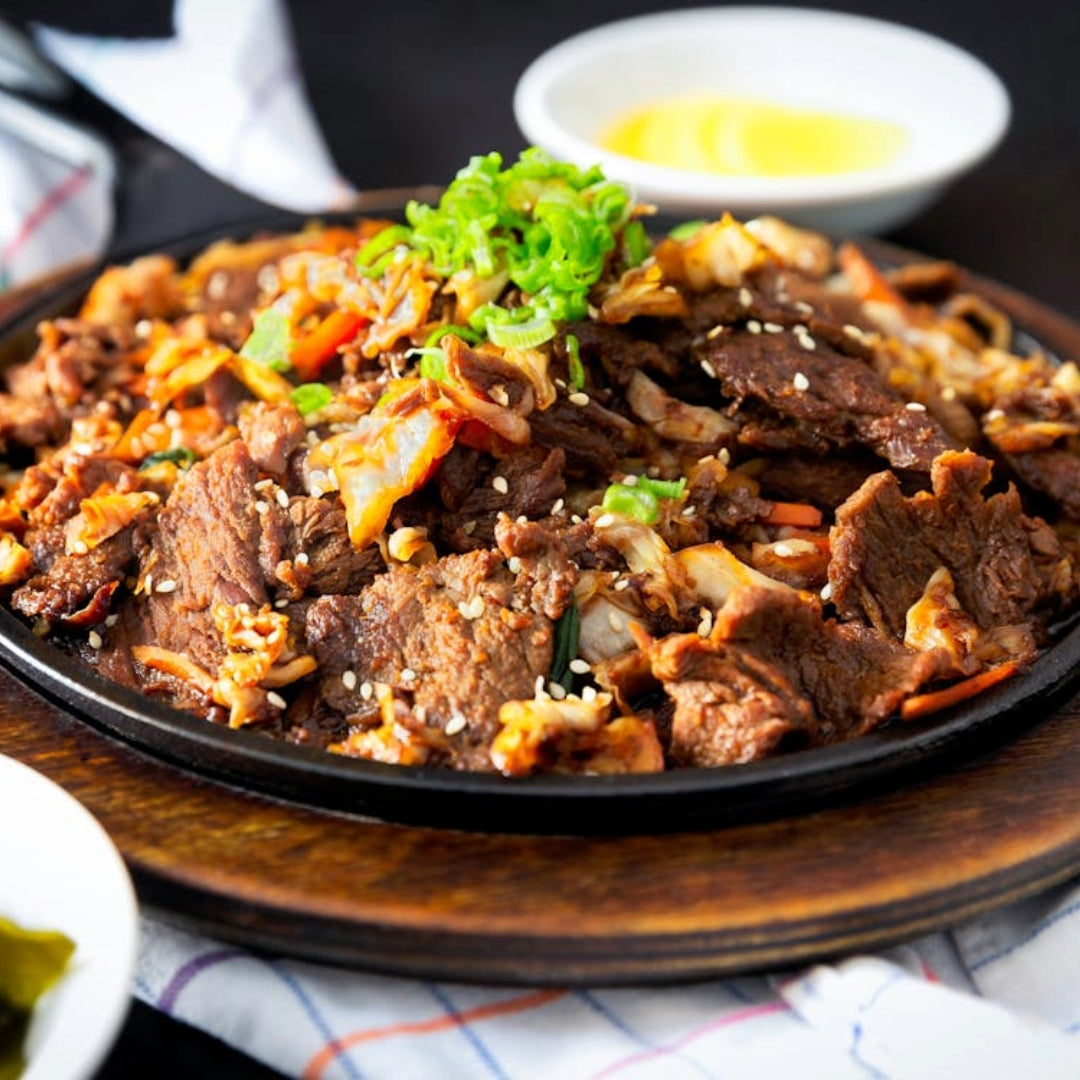 Sliced marinated beef bulgogi on a sizzling cast-iron platter topped with green onions and sesame seeds