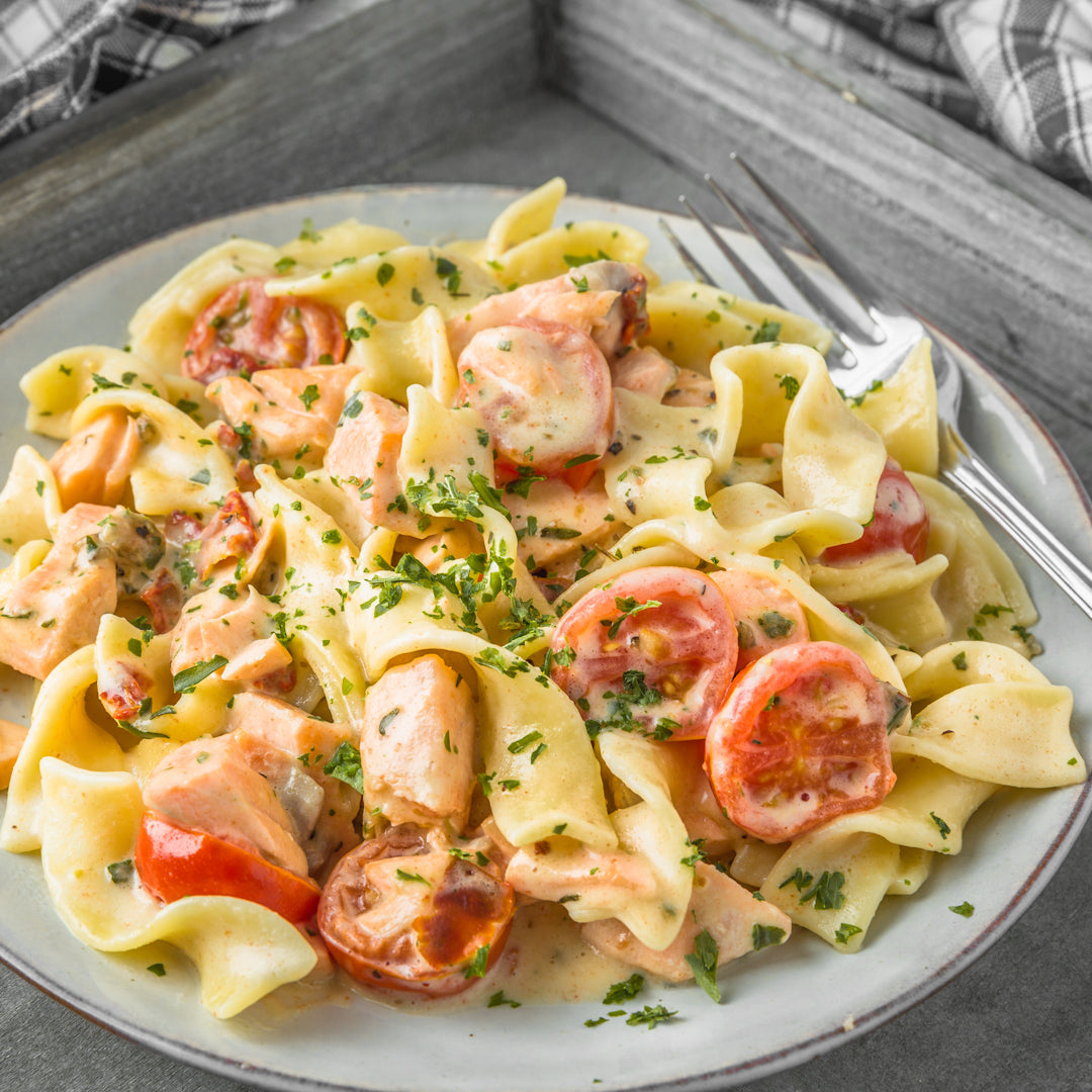 Creamy pasta with egg noodles, chunks of salmon, halved cherry tomatoes and chopped parsley on a plate with a fork.