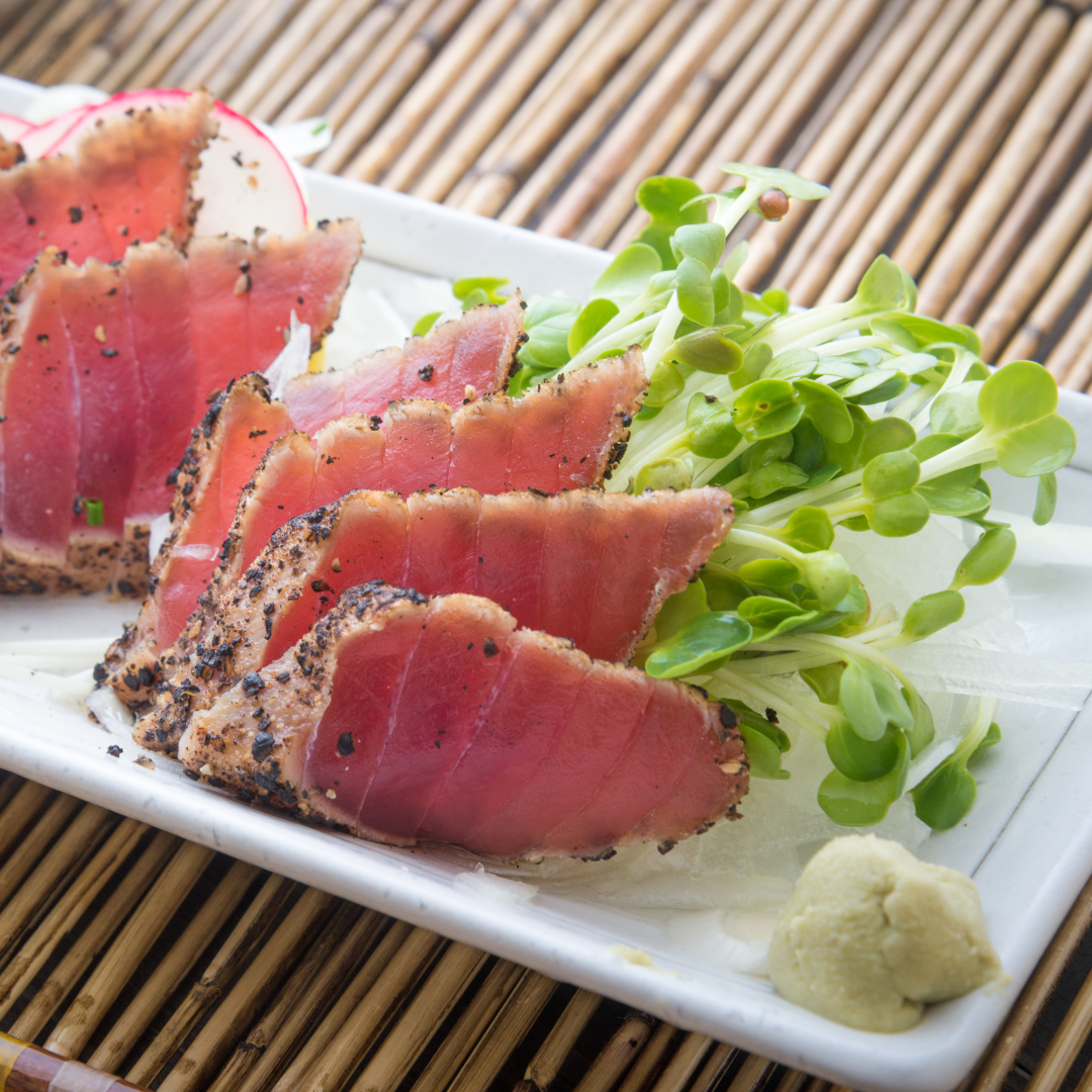Seared tuna tataki crusted with cracked black pepper, plated with sprouts and a wasabi dollop.