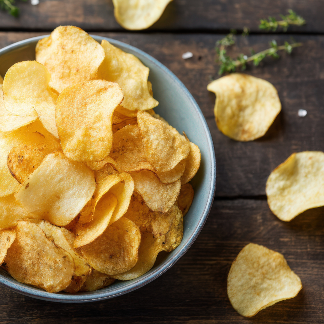 Close up of bar chips showcasing golden crisp slices in a bowl with scattered chips and herbs on a dark wooden table