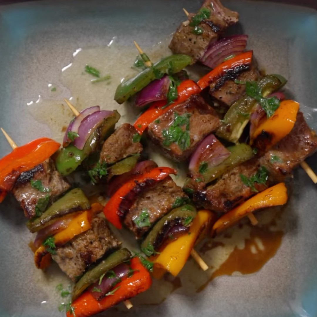 Top-down view of steak skewers with grilled steak, colorful peppers, red onion, and parsley on a gray plate