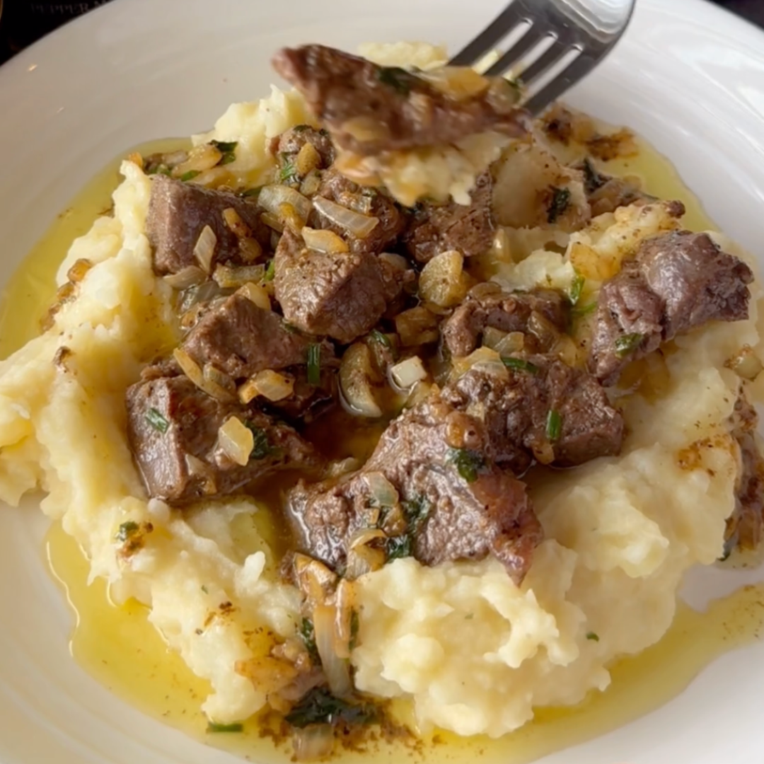 Close-up of garlic herb butter steak bites over mashed potatoes with herbs and melted butter on a white plate