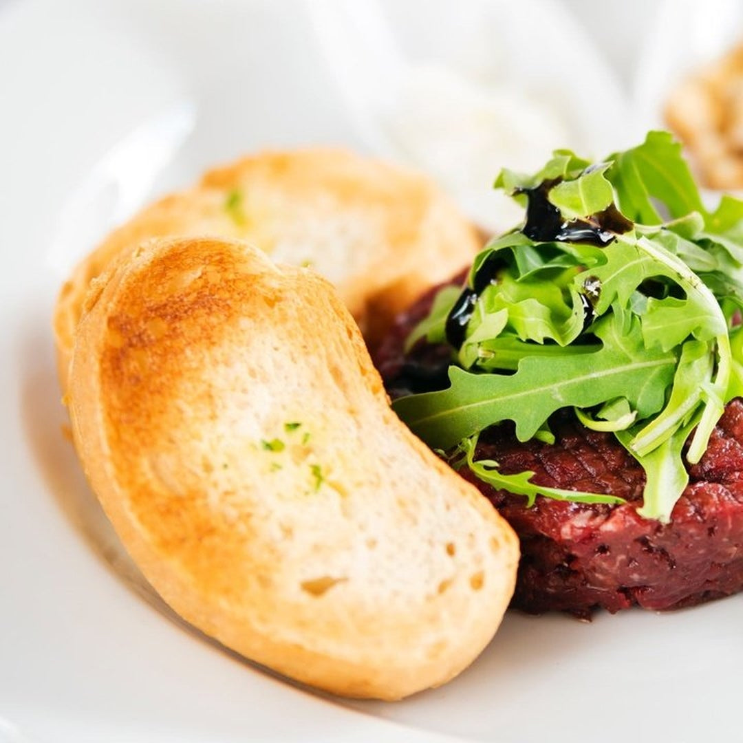 Beef filet mignon steak tartare topped with greens and served with toasted baguette slices.