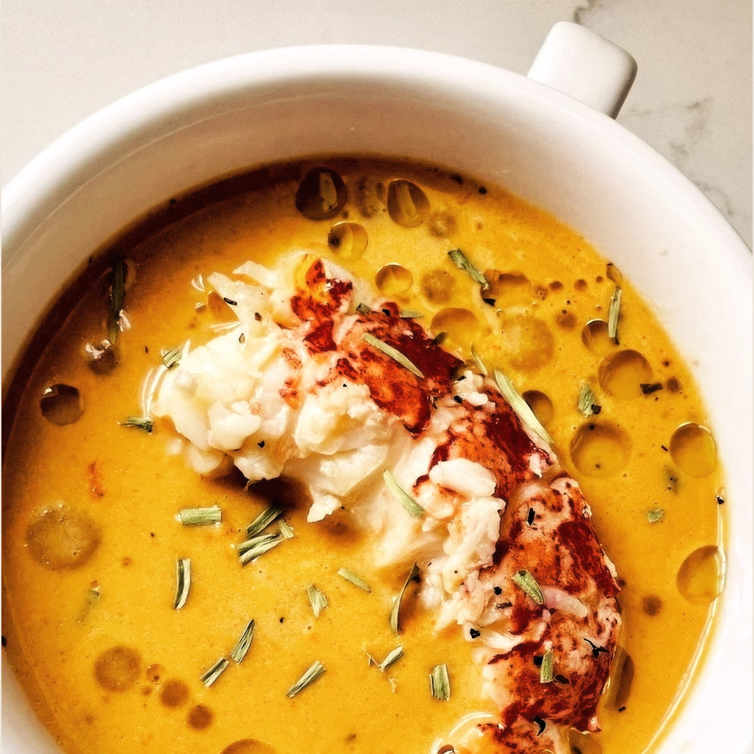 Savory lobster bisque in a white bowl topped with lobster meat and chopped herbs.