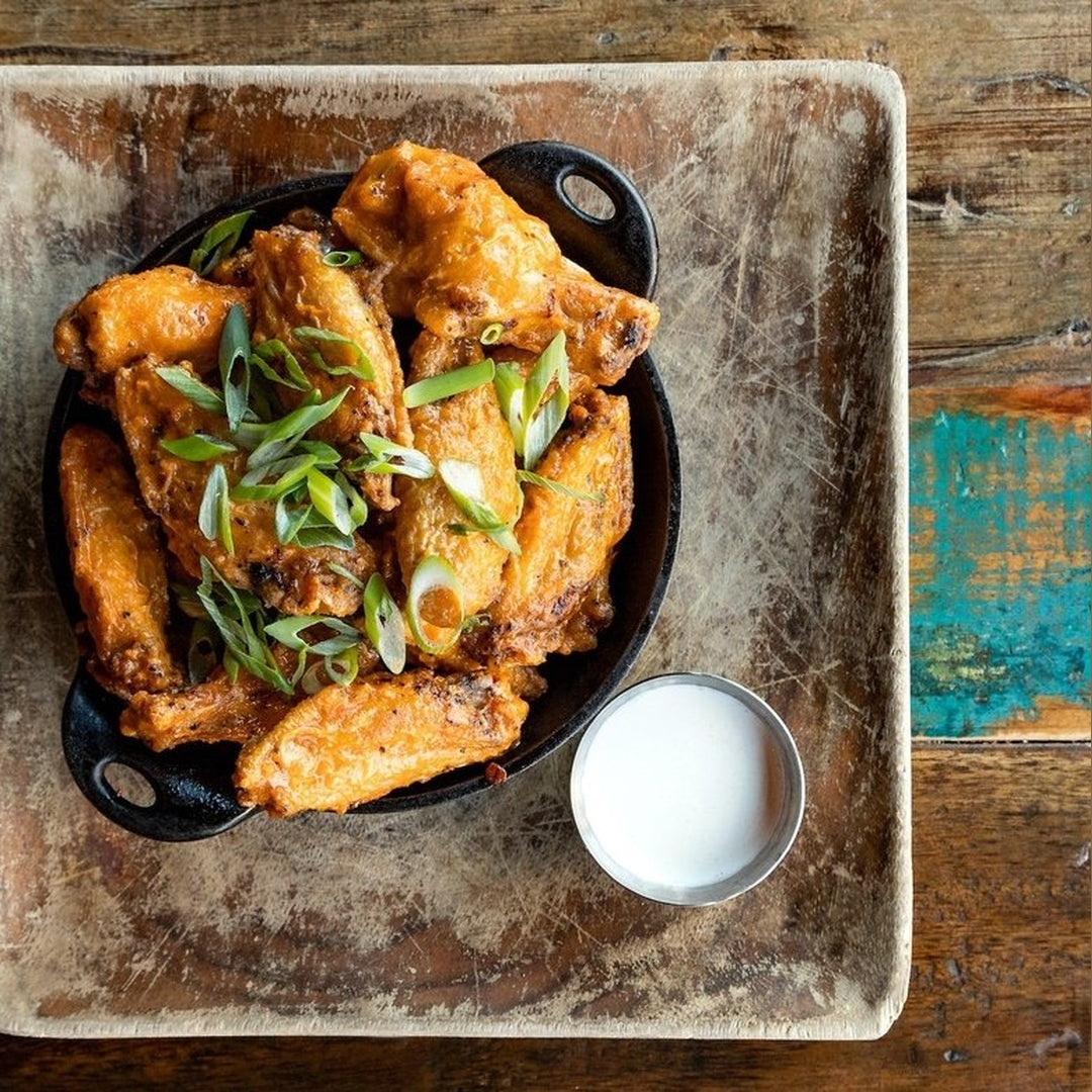 Crispy lemon pepper chicken wings in a cast iron skillet with green onions and a small ramekin of white dipping sauce.