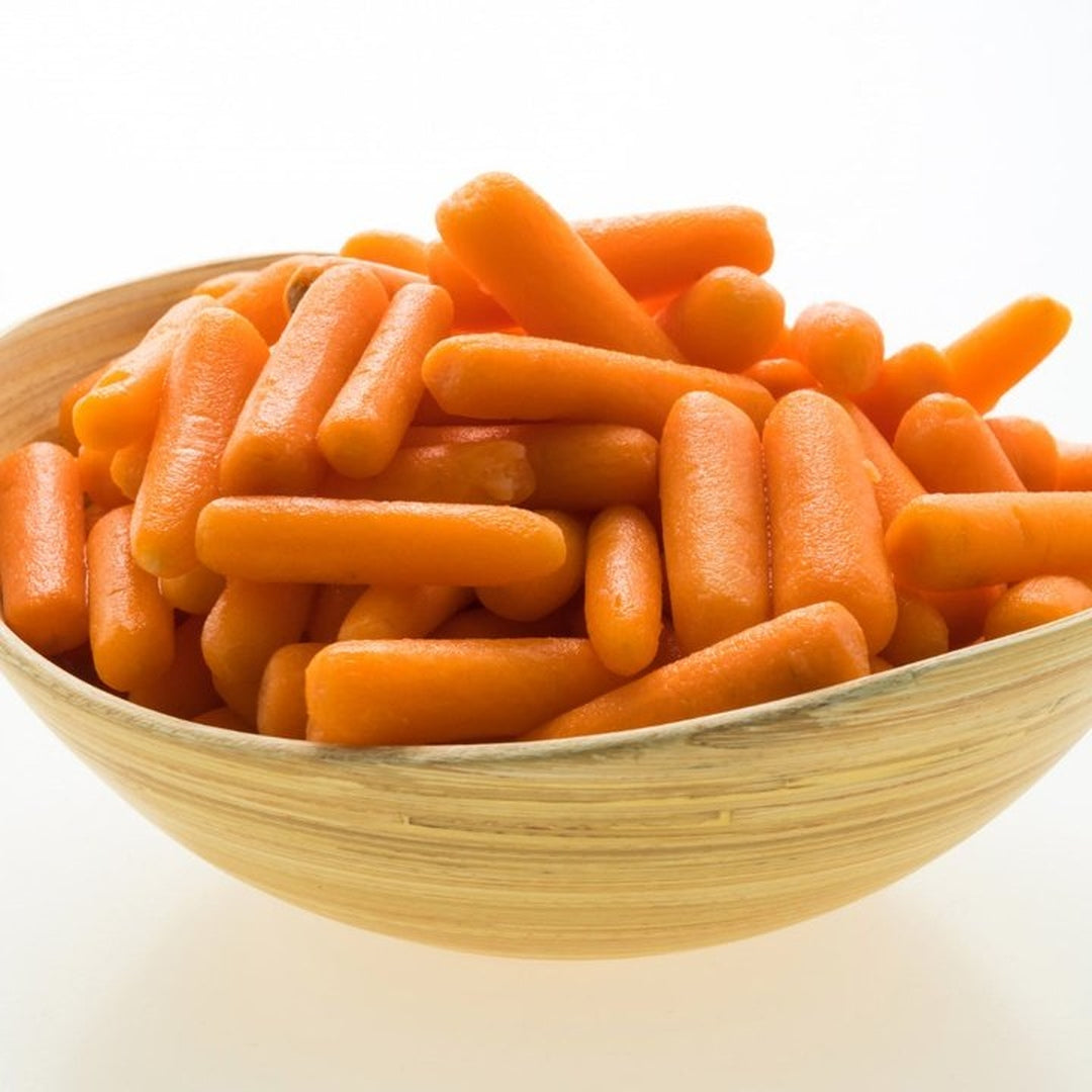Bright orange baby carrots piled in a light wood bowl