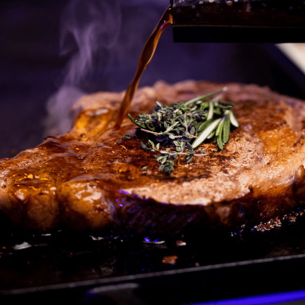 Juicy steak being basted with au jus as a sprig of thyme rests on top.