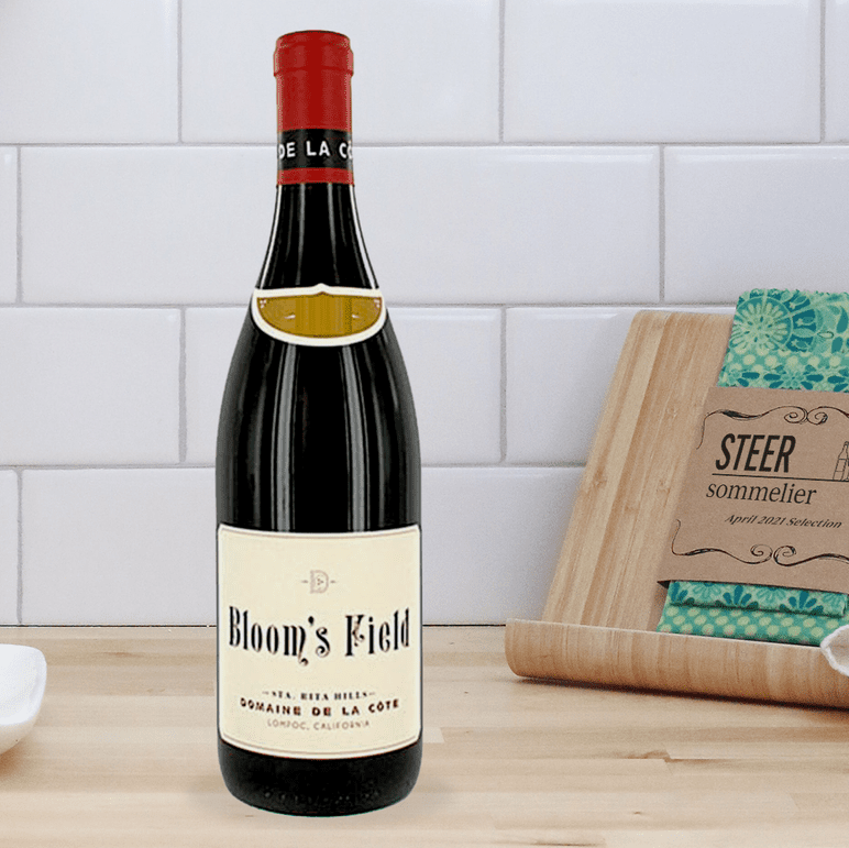 Bloom's Field Pinot Noir bottle on a wooden countertop with white subway tile backdrop.