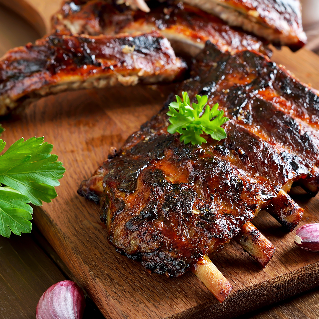 Bone-in pork ribs with a glossy dark glaze on a wooden cutting board, garnished with parsley.